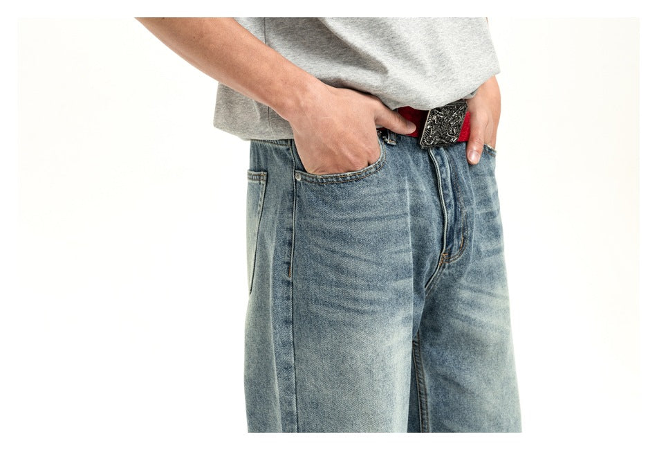 Close-up of the jeans' front pockets, faded light-wash denim, red belt and ornate buckle.