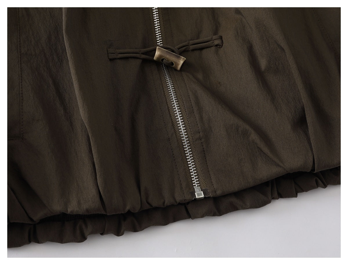 Close-up of a dark olive-brown jacket showing its silver front zipper, toggle detail, and gathered hem.