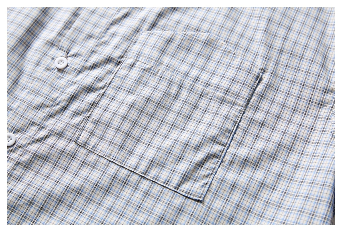 Close-up of a square chest pocket and buttons on a light blue, gray, and tan plaid shirt.