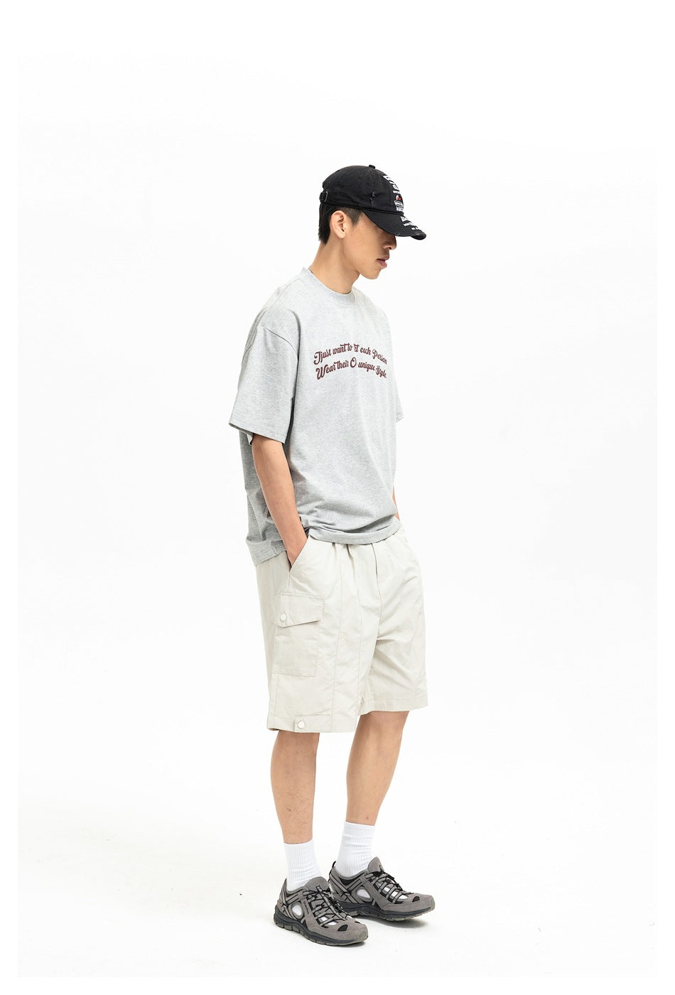 Side view of a model wearing a light gray script T-shirt and cream cargo shorts.
