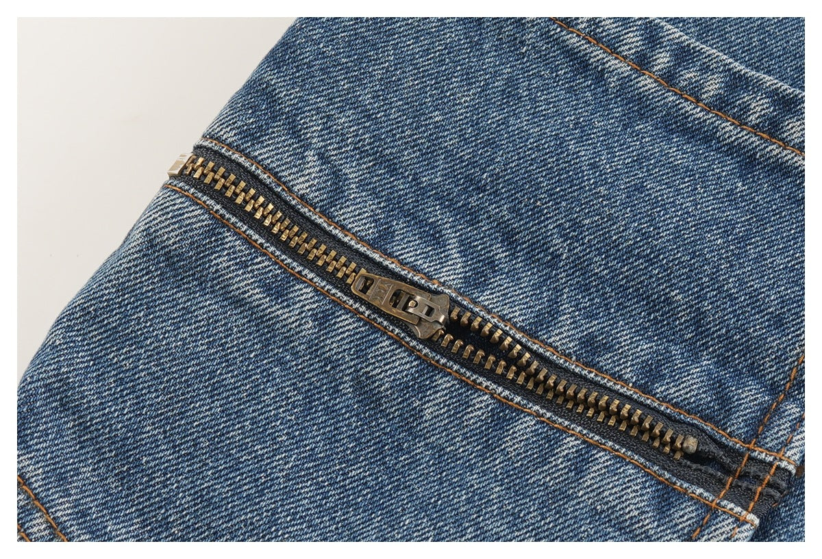 Close-up of a brass-colored zipper and stitching on blue denim.