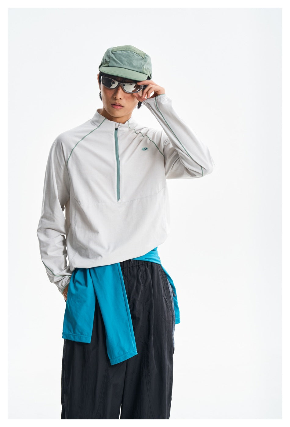 Closer view of a model wearing a white teal-trim zip-neck pullover and black pants with a turquoise layer tied at the waist.
