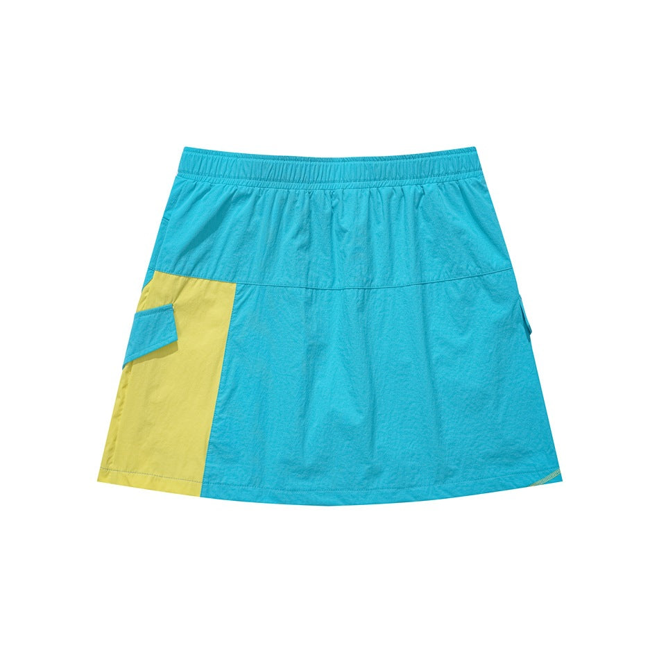 Front view of a turquoise A-line skirt with a yellow side panel, elastic waistband, and cargo-style pocket flaps.