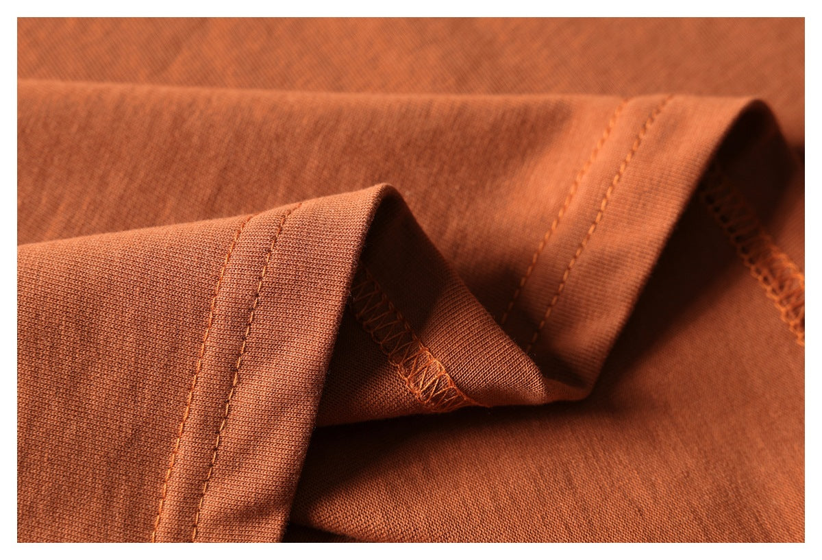 Close-up of rust-orange garment fabric with a folded edge, double stitching, and overlocked seam.