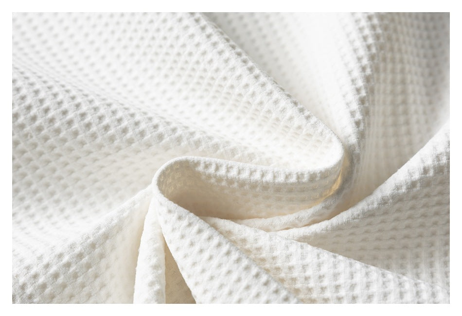 Close-up of white fabric with a raised waffle-like texture, softly folded.
