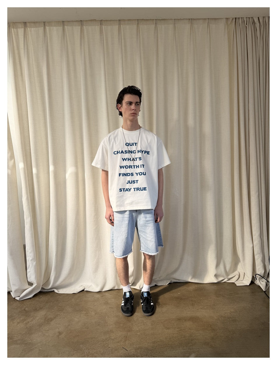 Model wearing the off-white slogan T-shirt with light denim shorts and black sneakers, front view against a cream curtain