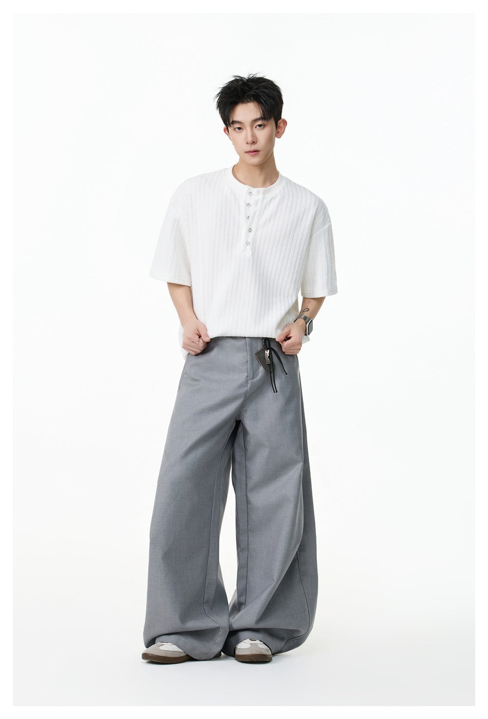 Model wearing a white short-sleeve ribbed Henley shirt with a button placket and gray wide-leg trousers.