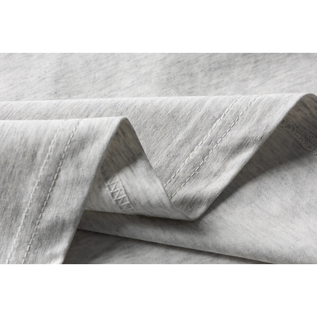 Close-up of the double-stitched hem and overlock seam on a light gray heather T-shirt.