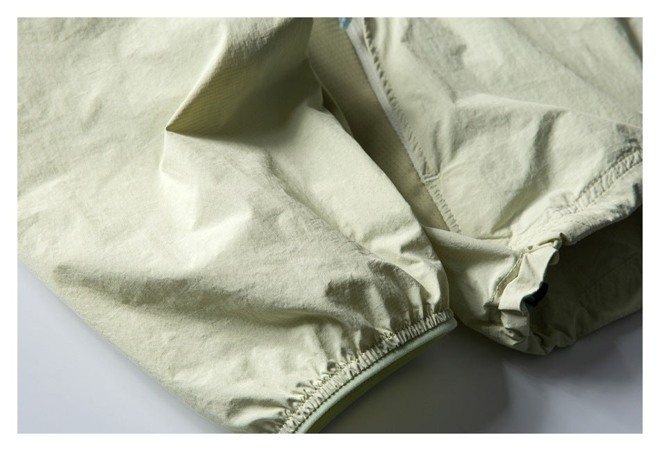 Close-up of pale sage jacket fabric showing a gathered elastic cuff and adjacent seam details.