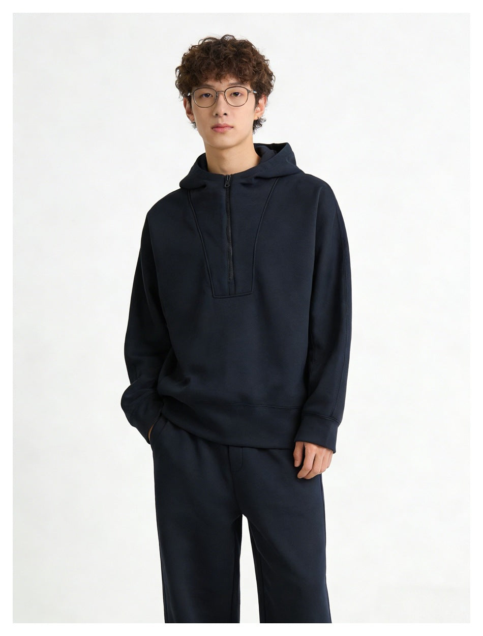 Front view of a model wearing a dark navy hooded pullover with a short zipper and matching pants.