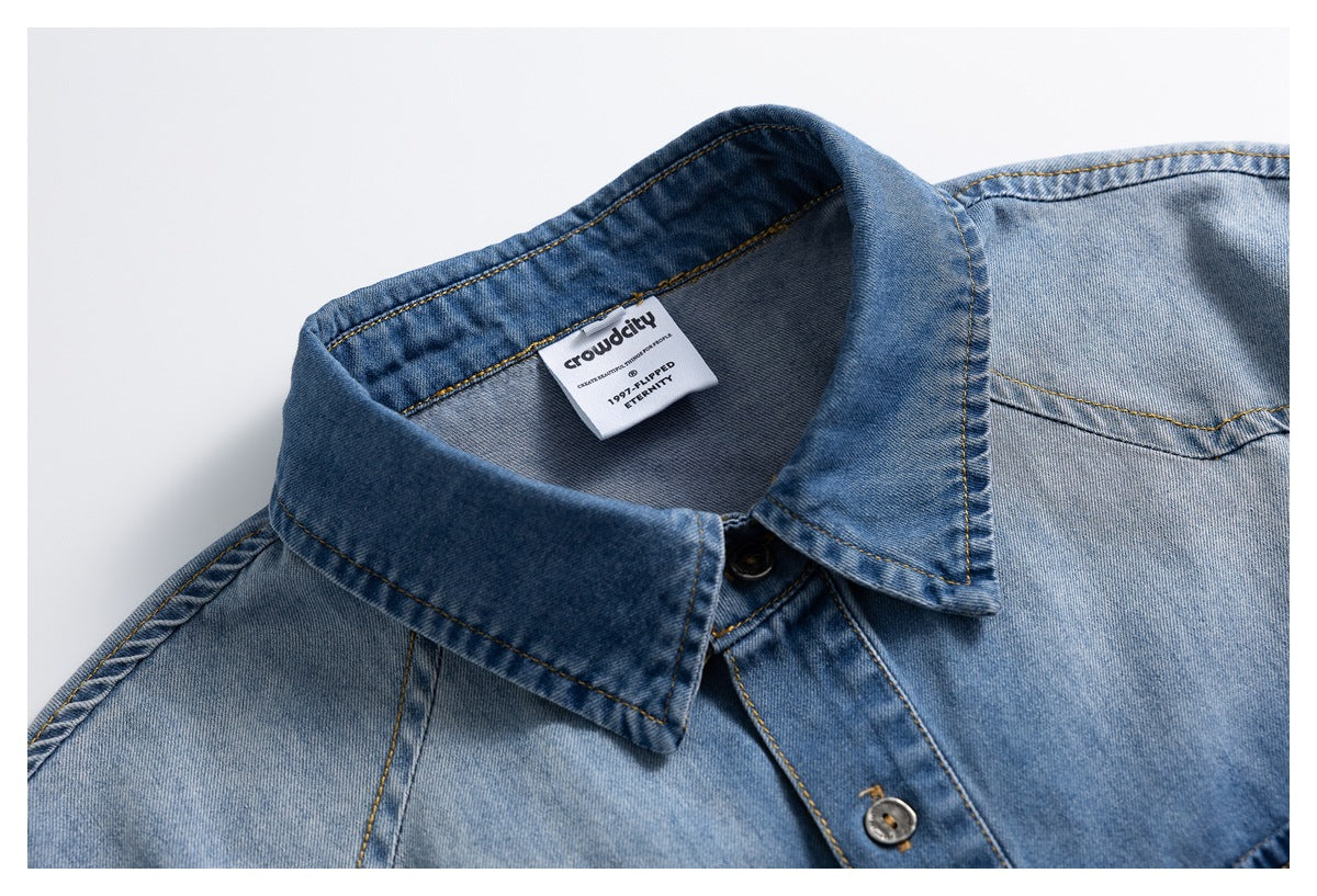 Close-up of a light blue denim shirt collar, button placket, contrast stitching and interior neck label.