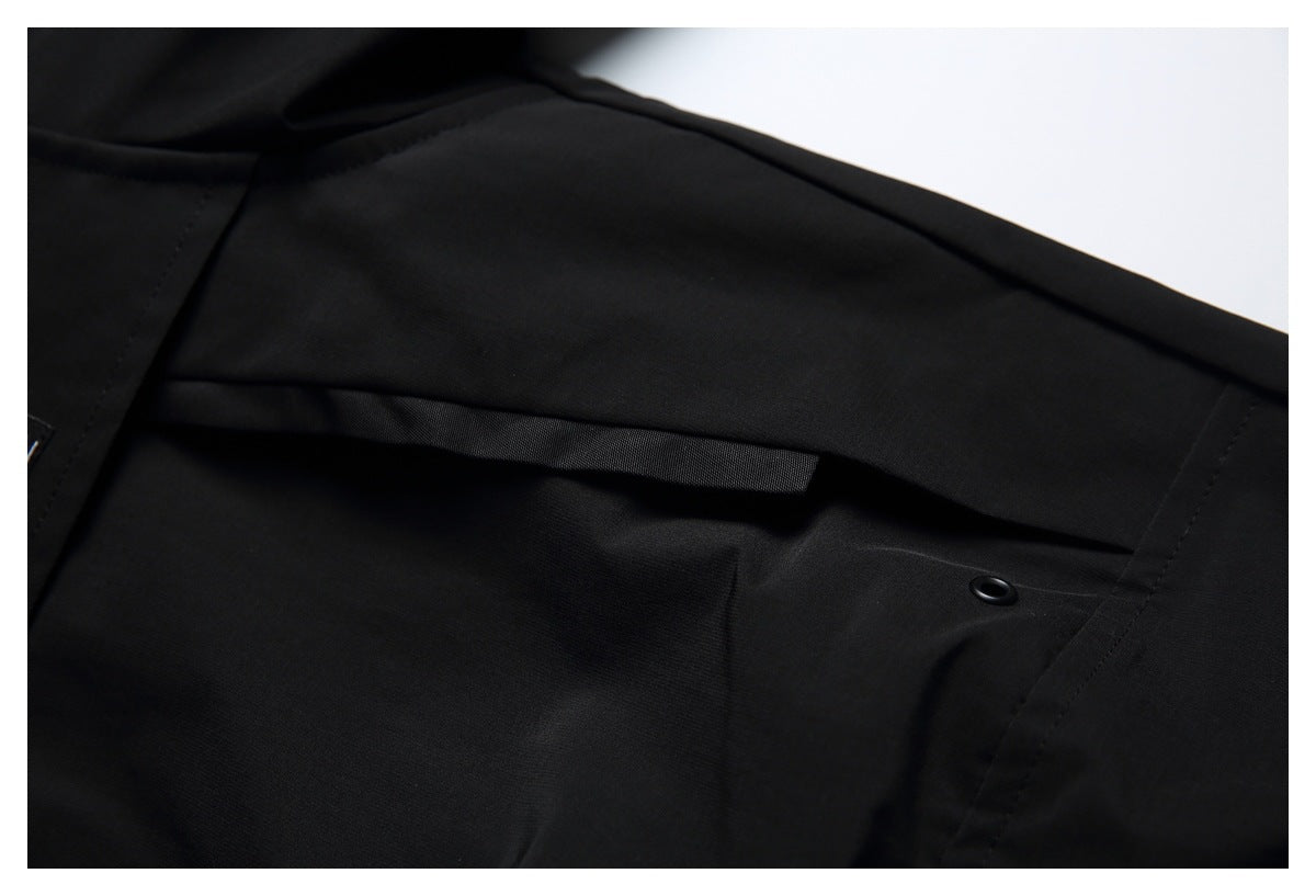 Close-up of a black garment with a horizontal fabric flap, stitched seams, and a small black eyelet.