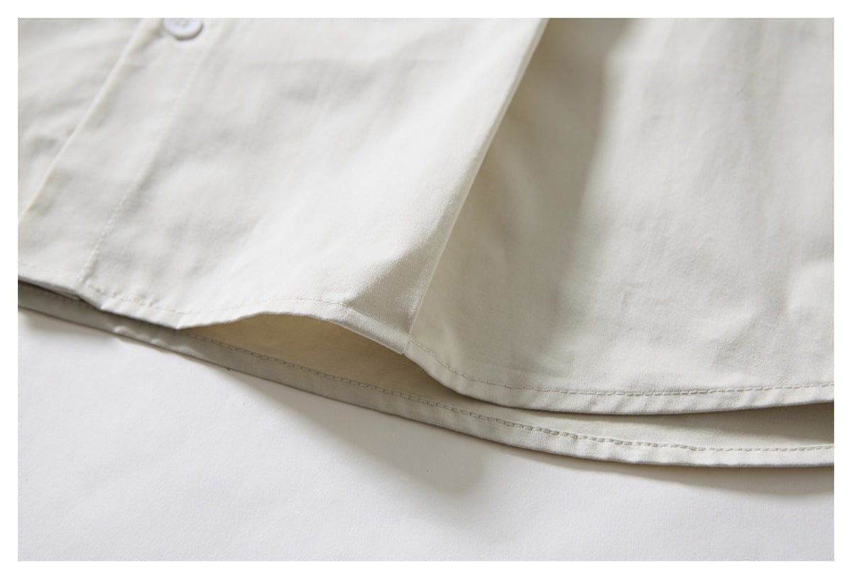 Close-up of the curved double-stitched hem of an ivory shirt.