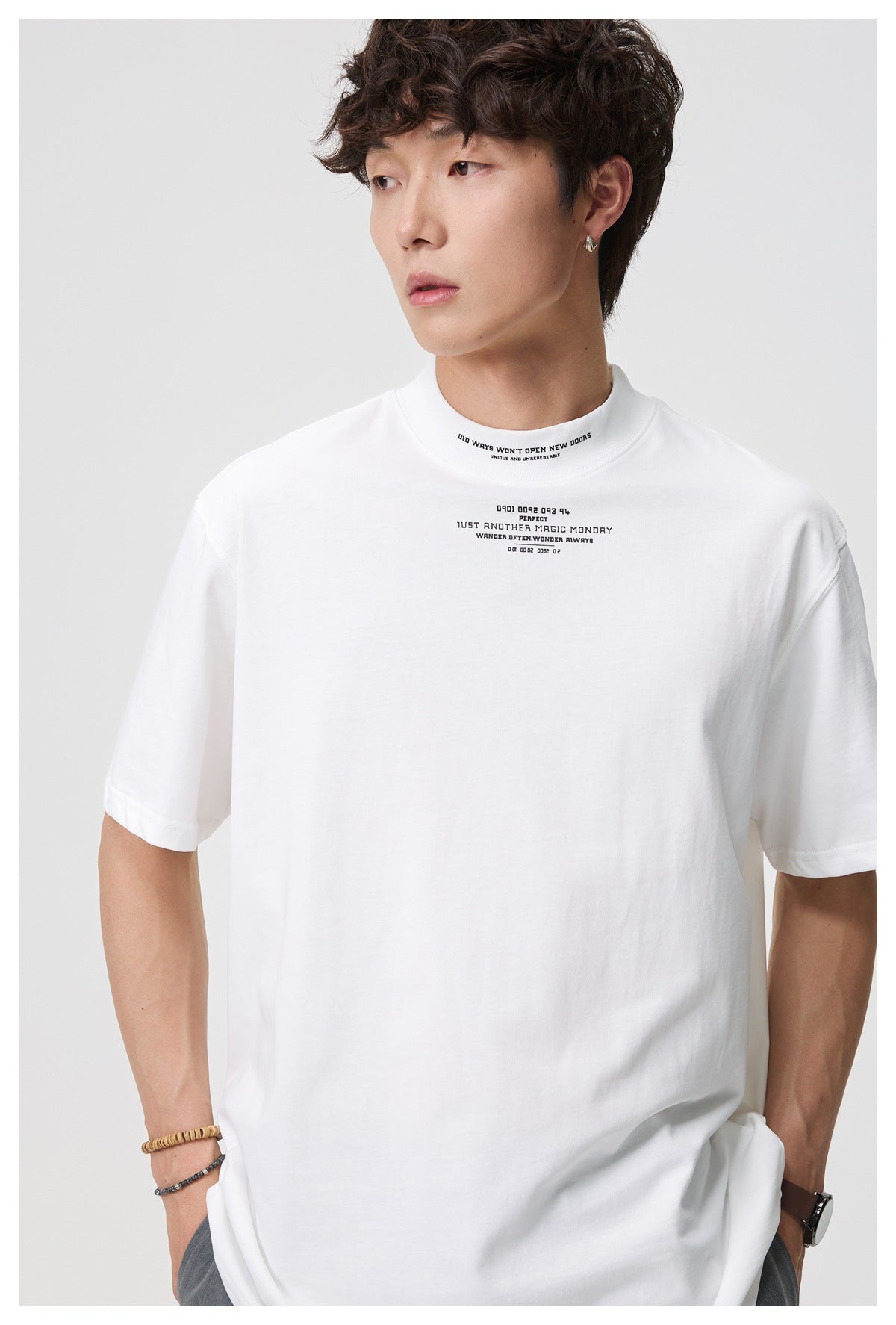 Close-up of a man wearing a white mock-neck T-shirt with small black text print on the collar and chest