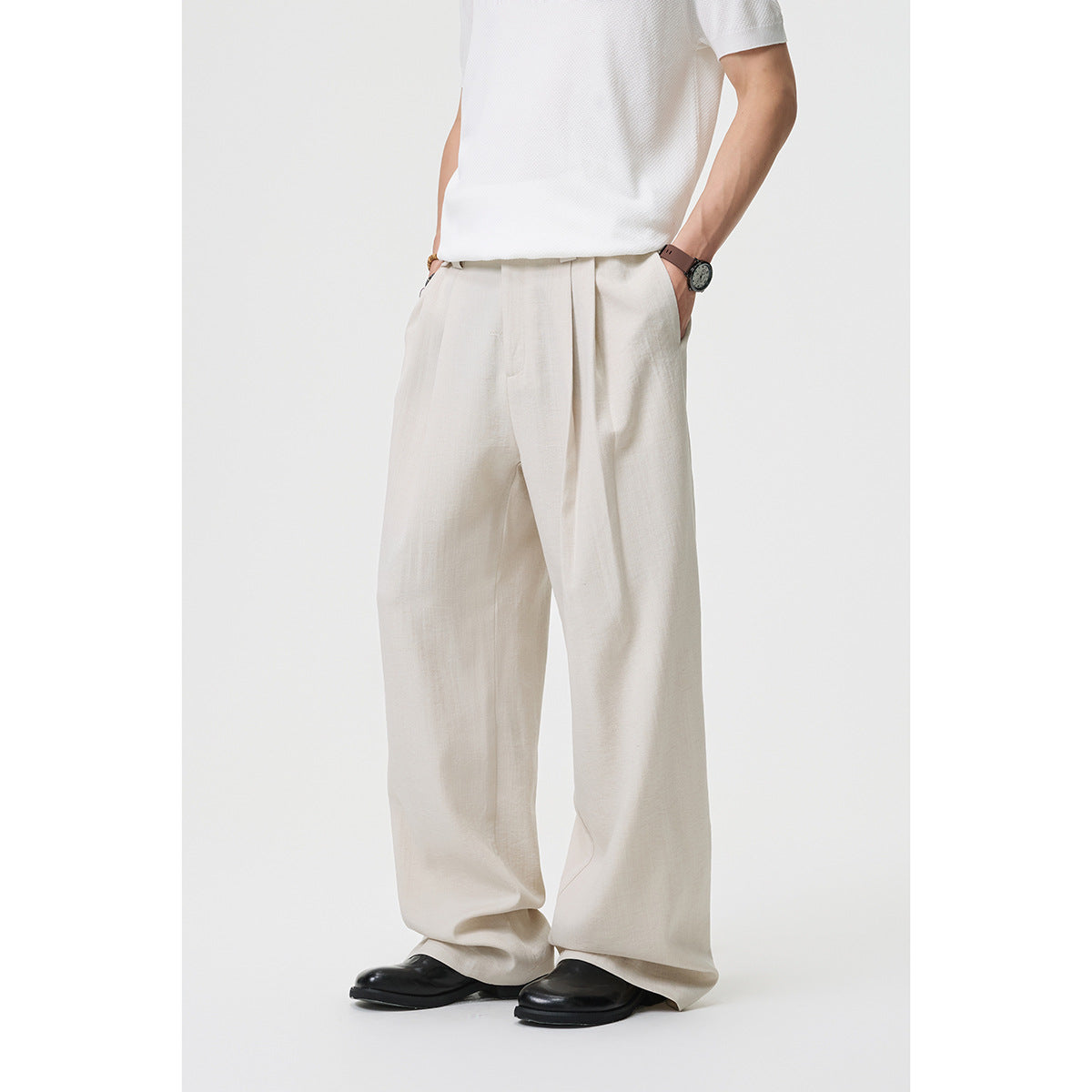 Cropped front view of a model wearing loose ivory trousers with a white top; pleats and wide legs are visible.
