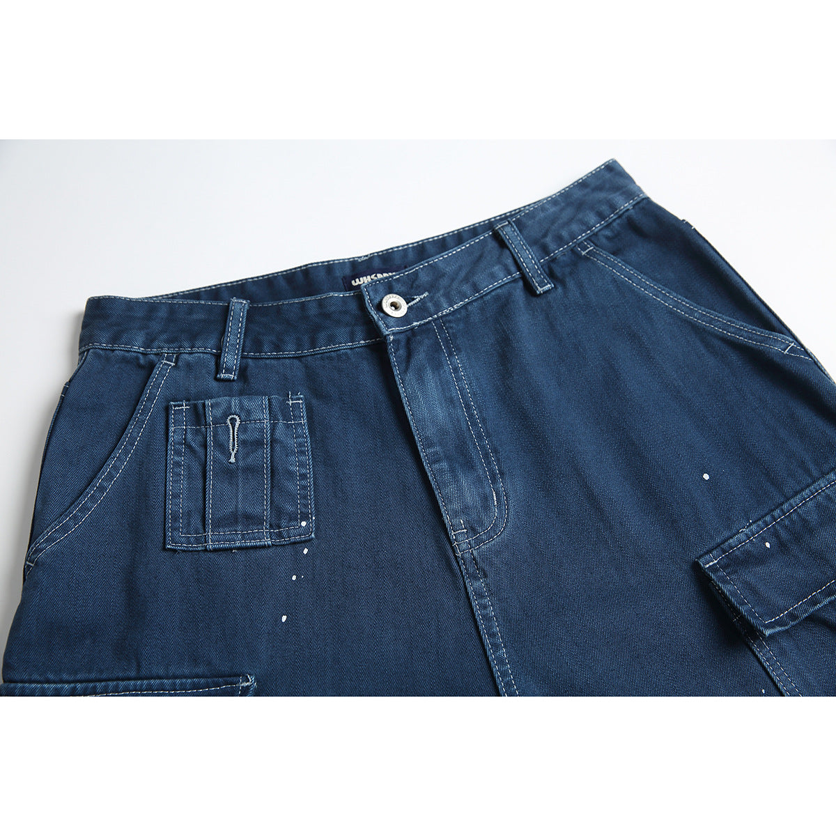 Close-up of dark blue denim cargo shorts showing the waistband, button, front pockets, and white paint-like speckles.