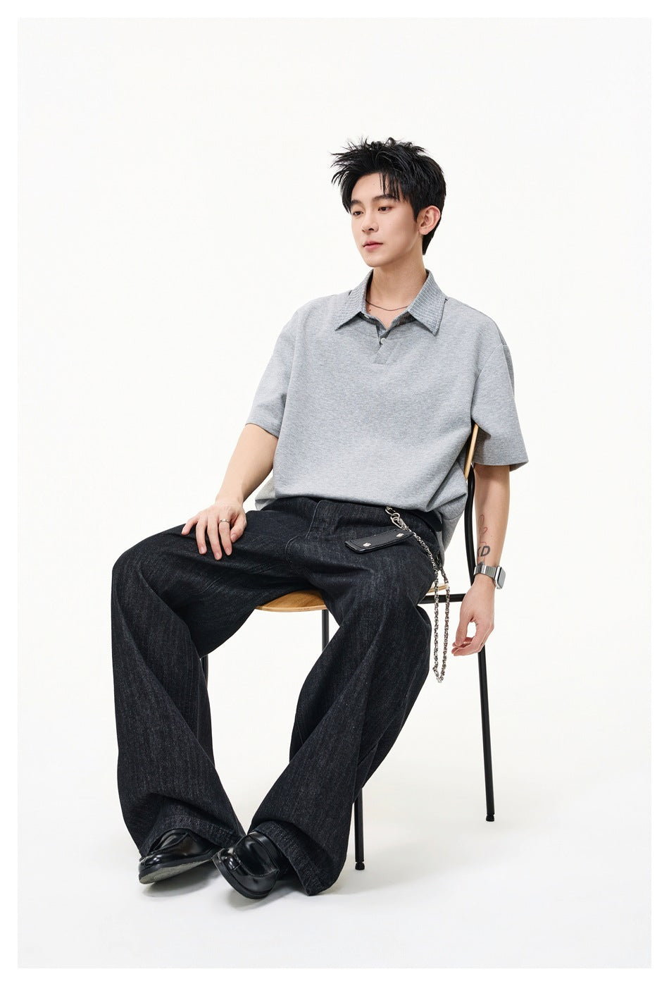Seated model wearing an oversized light gray short-sleeve polo shirt and dark wide-leg jeans.