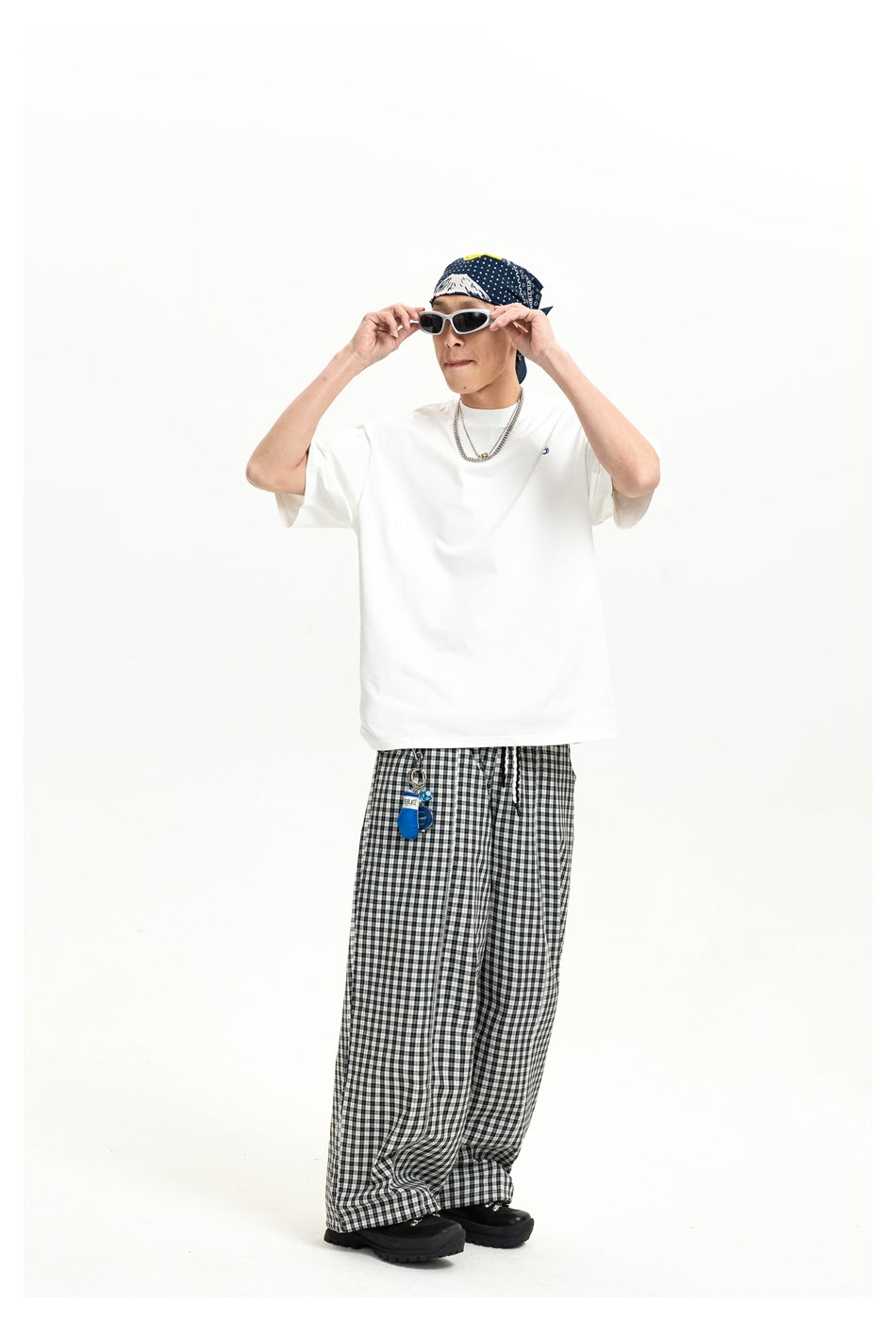 Person wearing white short-sleeve crew-neck T-shirt with small chest logo, checked pants, bandana and sunglasses