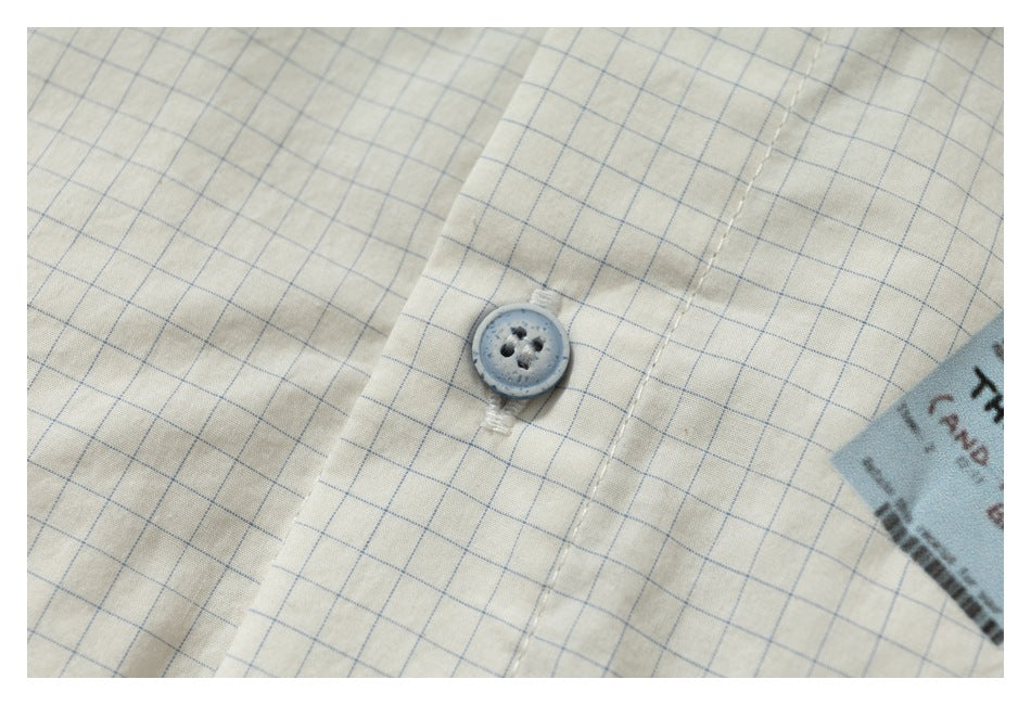 Close-up of a gray button and stitched placket on cream fabric with a fine blue grid.