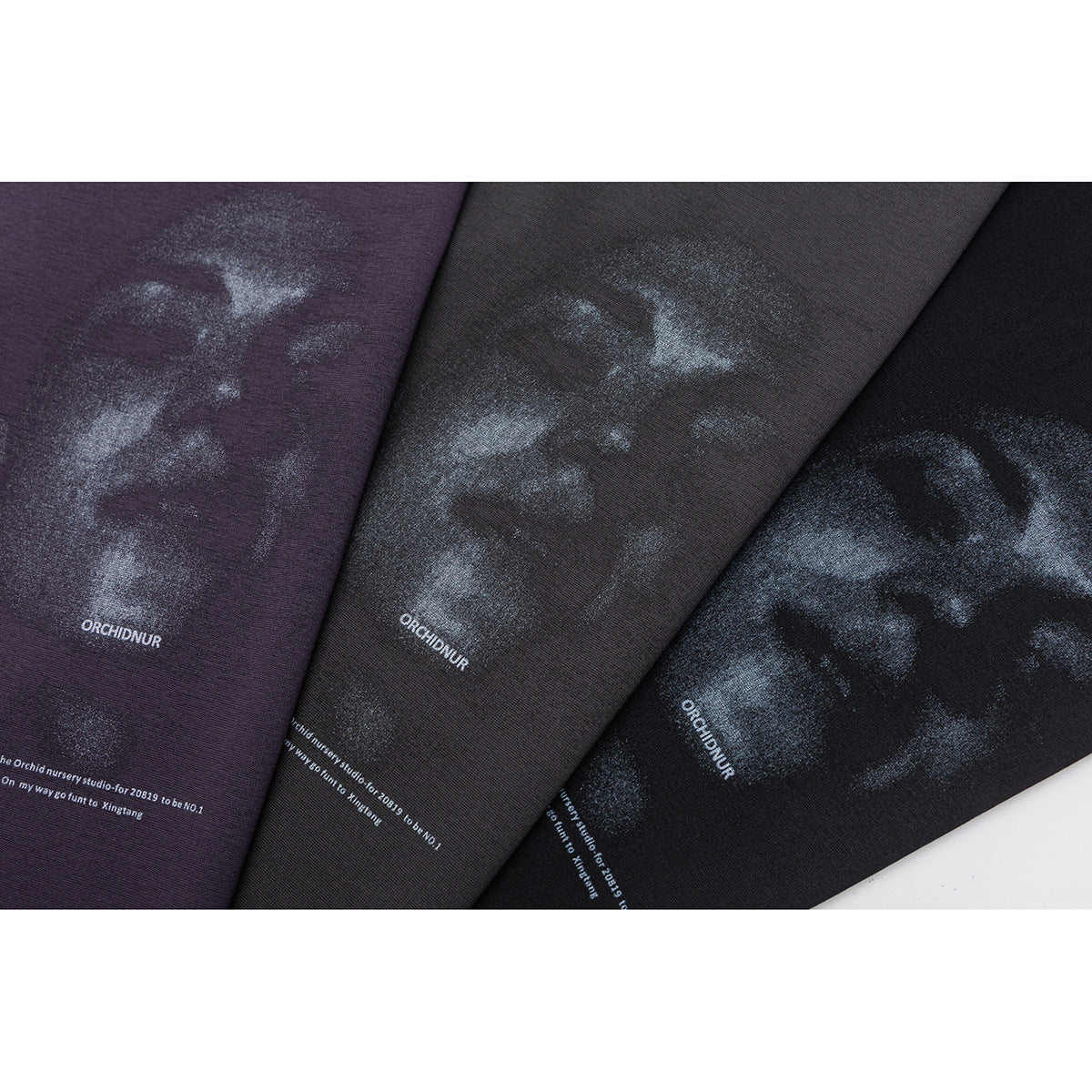 Close-up of three dark purple, charcoal, and black fabrics with a pale printed graphic and small English text.