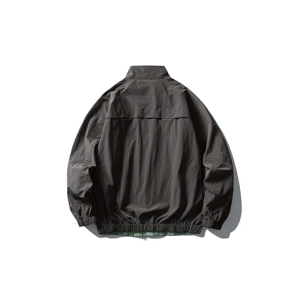 Back view of a charcoal gray jacket with a high collar, back vent flap, and elastic cuffs and hem; green shows below the hem.