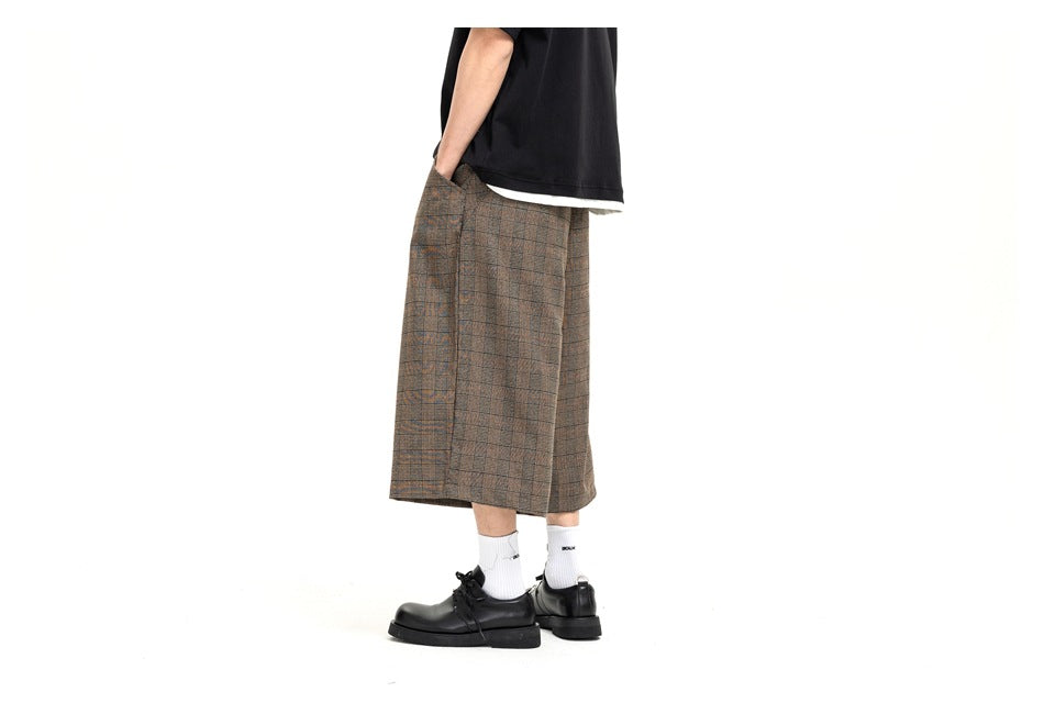 Side view of a model wearing brown plaid wide-leg shorts with a black T-shirt, white socks, and black shoes.