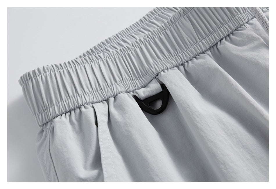 Close-up of the gathered elastic waistband and black loop detail on light gray shorts.