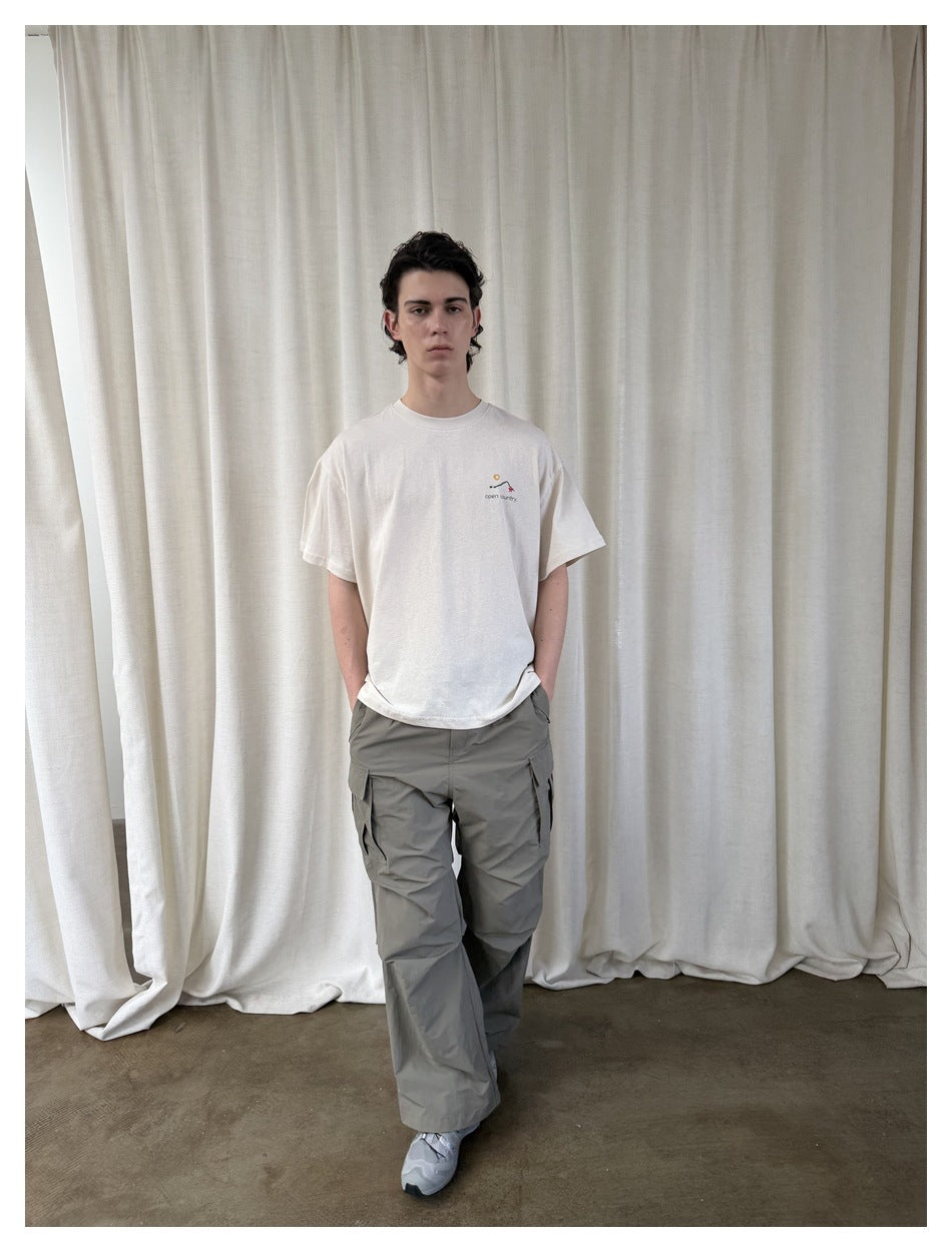 Model wearing a white short-sleeve T-shirt with a small chest graphic and gray cargo pants.