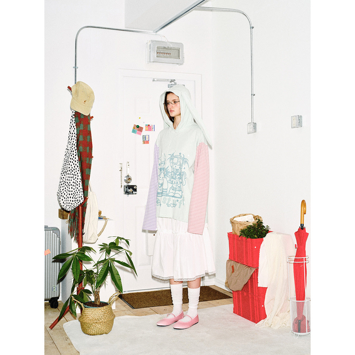 Full-length model wearing a pale mint graphic hoodie with long hood panels and pink and lilac striped sleeves.