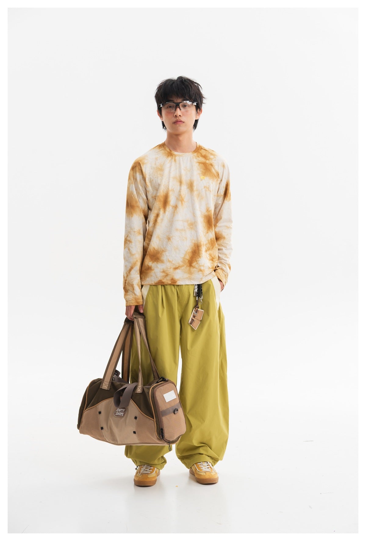 Model wearing a cream and ochre tie-dye long-sleeve shirt and loose yellow-green pants, shown from the front.