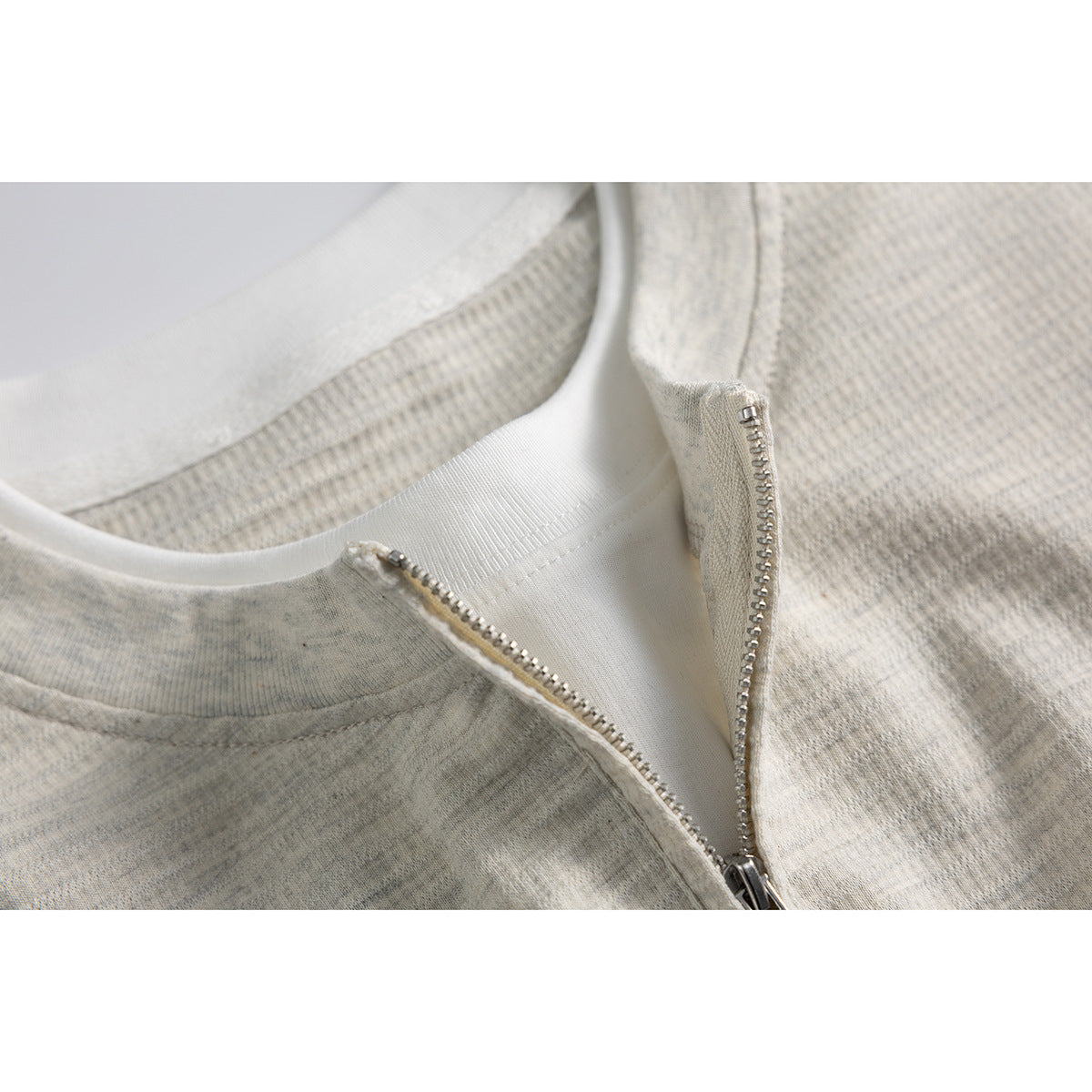Close-up of a light heather shirt with its quarter-zip partially open, showing the white inner collar.