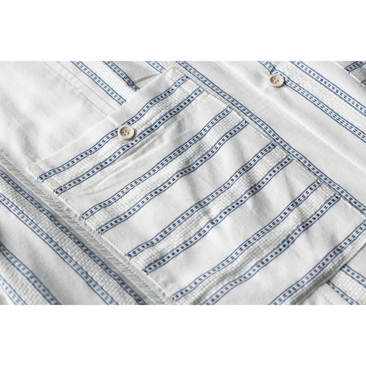 Close-up of a buttoned chest pocket on a white shirt with narrow blue patterned stripes.