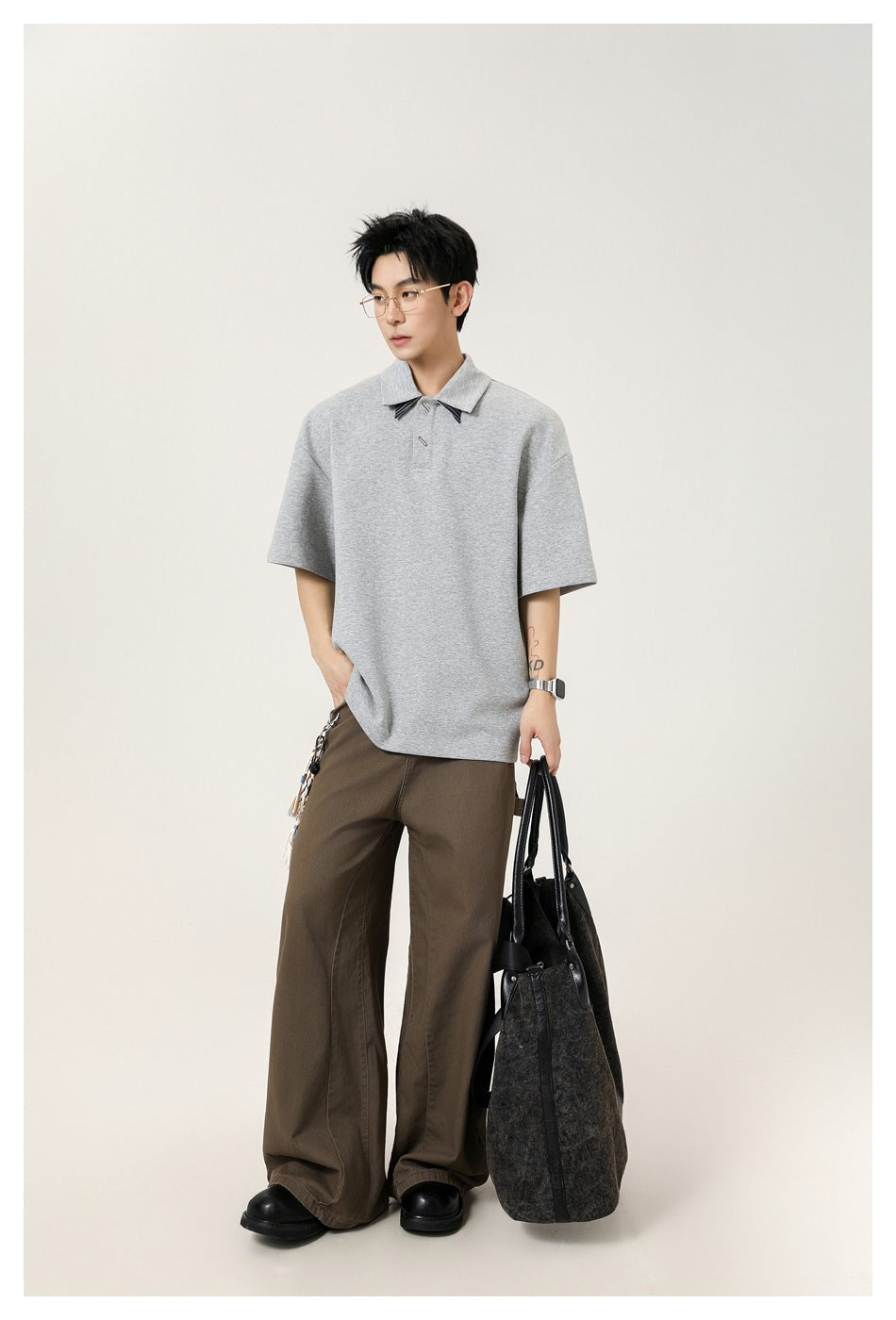 Model wearing an oversized light gray short-sleeve polo with a pointed collar and brown wide-leg trousers.