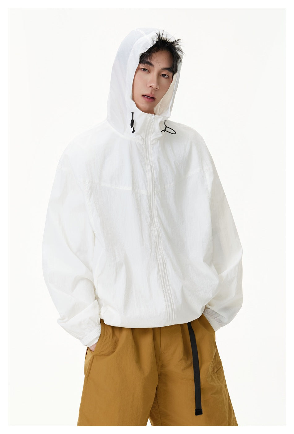 Closer view of a model wearing a white hooded zip jacket and mustard shorts, with the jacket hood up.