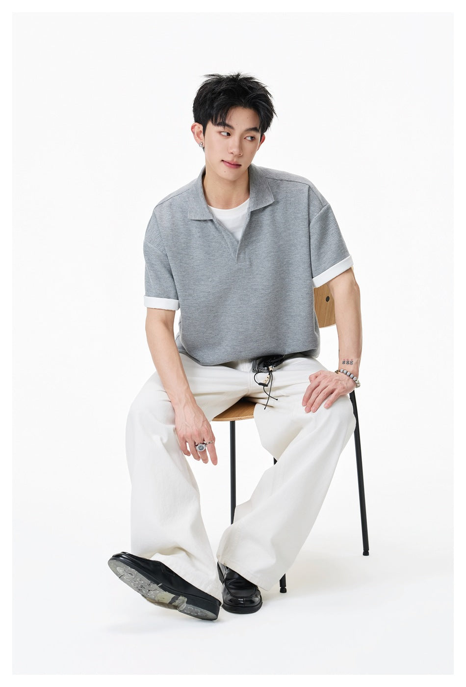 Seated model wearing a light gray short-sleeve collared shirt with white cuffs and loose white trousers.
