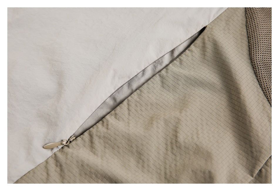 Close-up of a diagonal zipper pocket across pale beige and grid-patterned jacket panels.