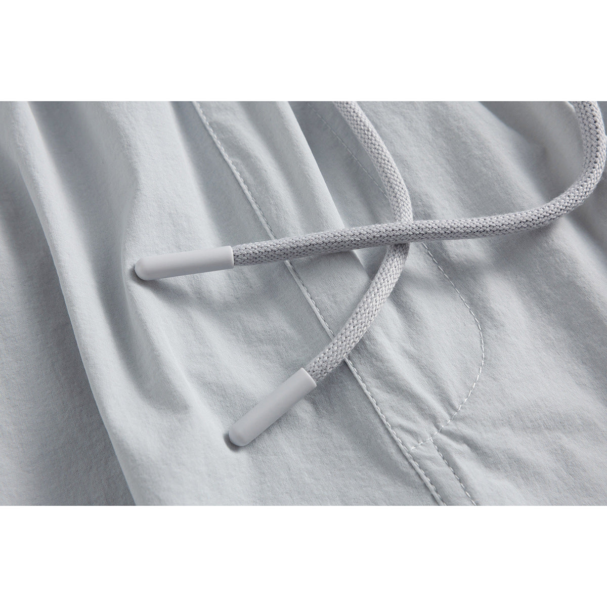 Close-up of light gray shorts with braided drawstrings and capped ends across the fabric.