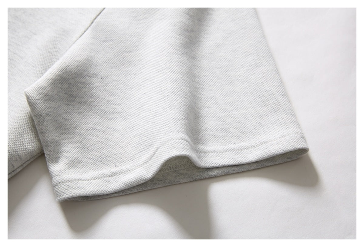 Close-up of a light gray knit polo shirt sleeve and stitched hem.