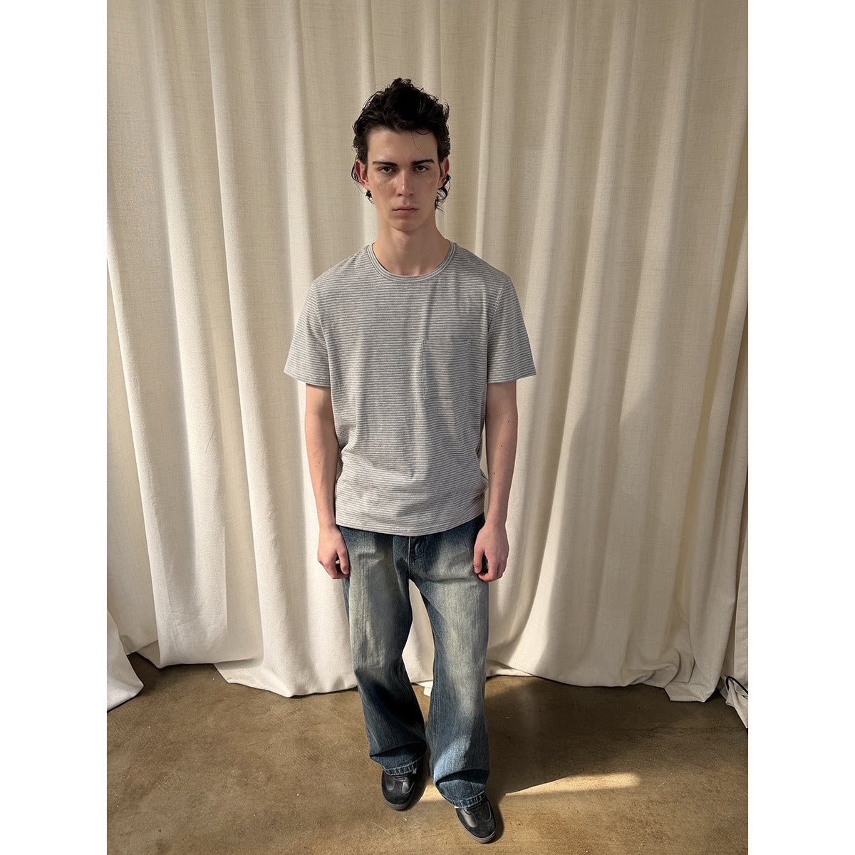 Model wearing a gray finely striped crew-neck T-shirt with a chest pocket and blue jeans.