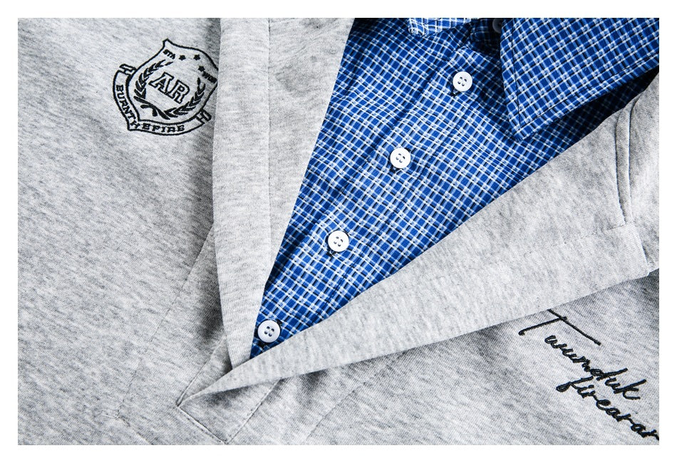 Close-up of a blue plaid button-up shirt beneath gray fabric, with white buttons and embroidered chest designs.