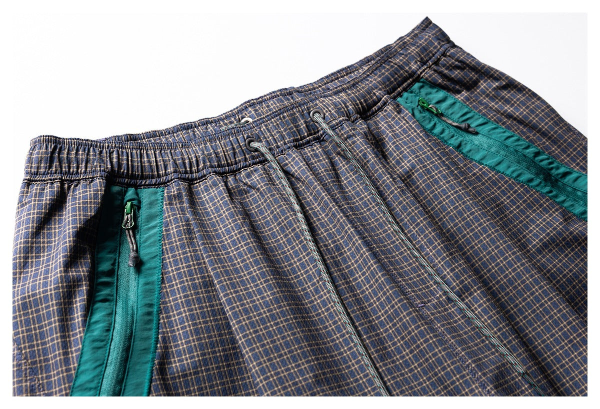 Close-up of navy plaid shorts with an elastic waistband, drawcord, and teal zippered pockets.