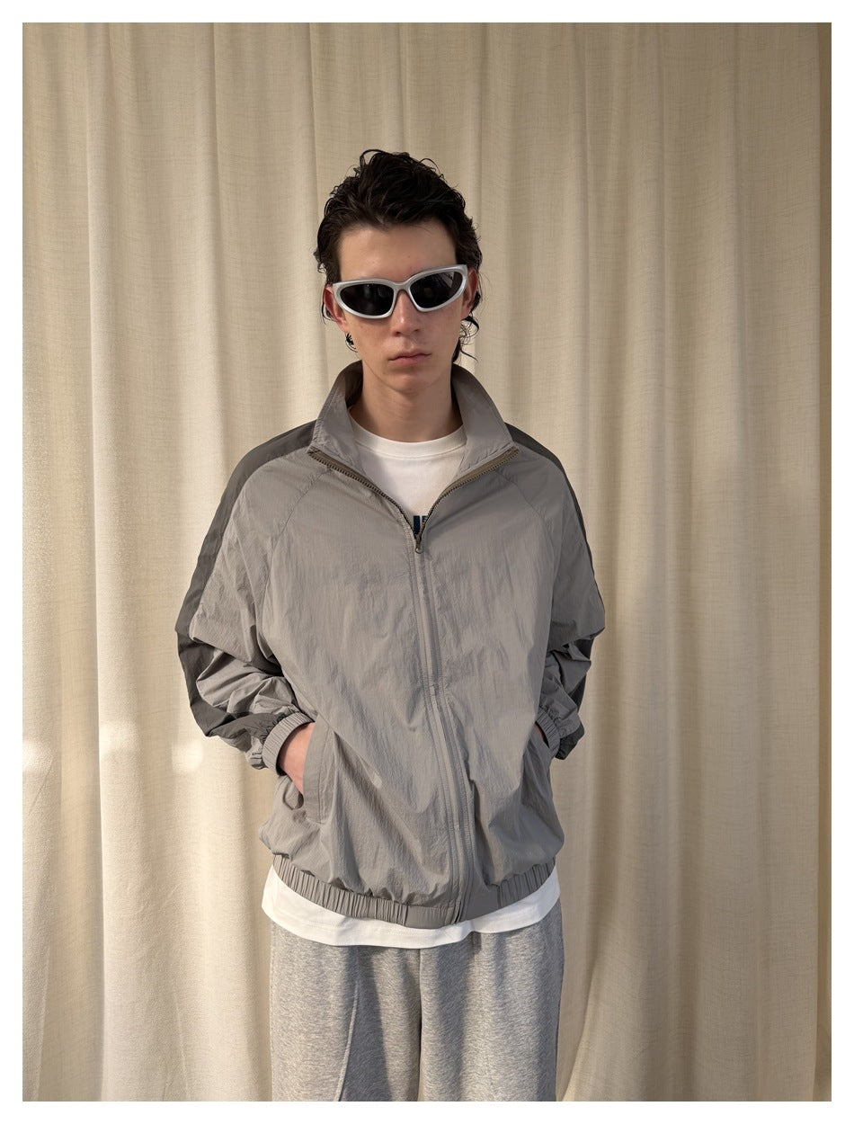 Front view of a model wearing a light gray zip-up jacket with dark shoulder panels and a stand collar.