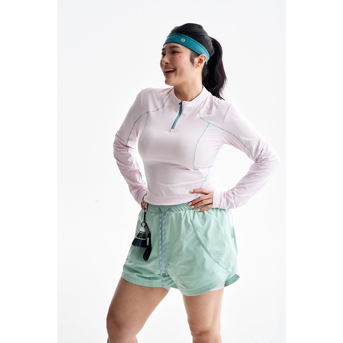 Model wearing a pale pink quarter-zip top with teal seams and mint-green running shorts.