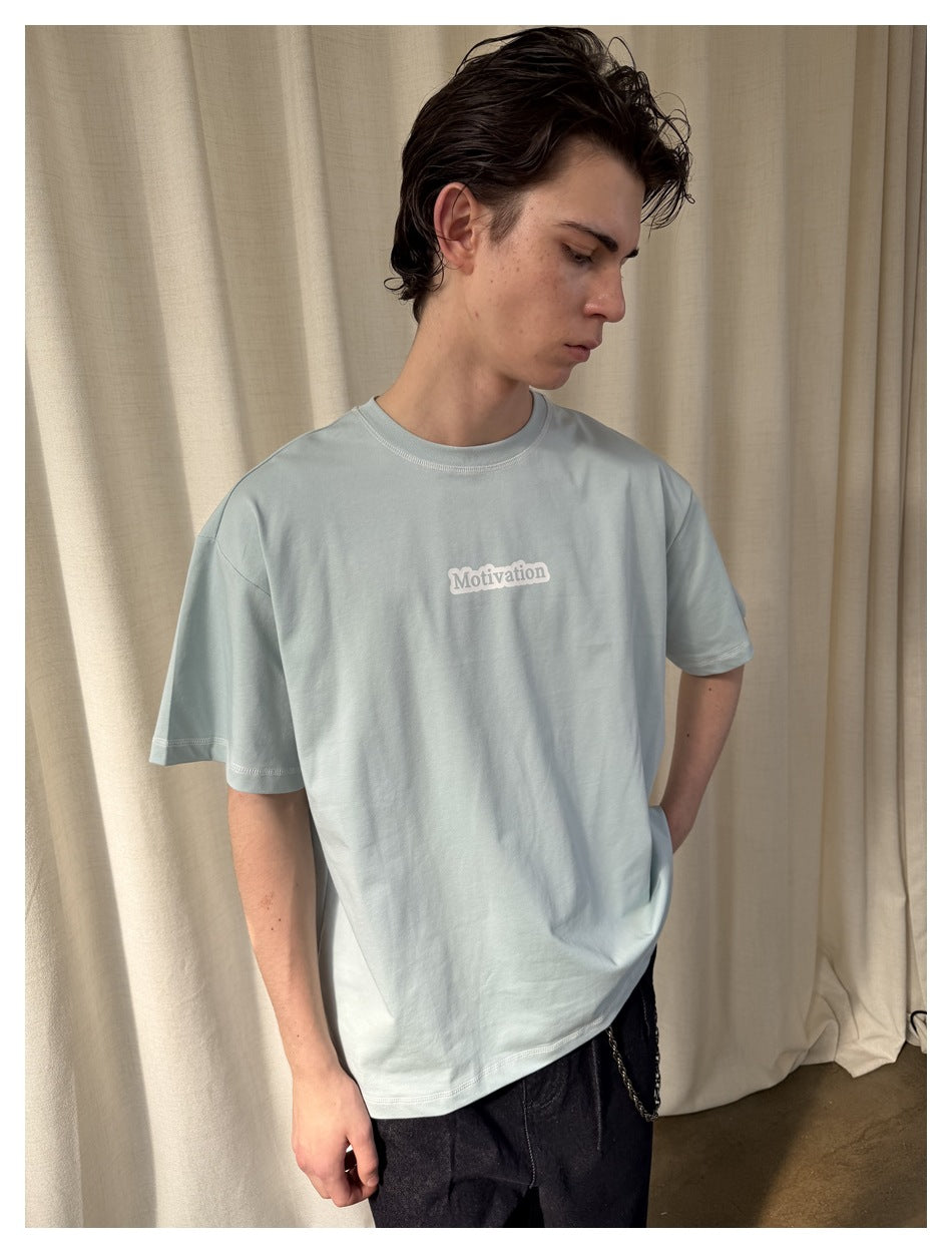 Model wearing a pale blue oversized T-shirt with a small white “Motivation” chest print.