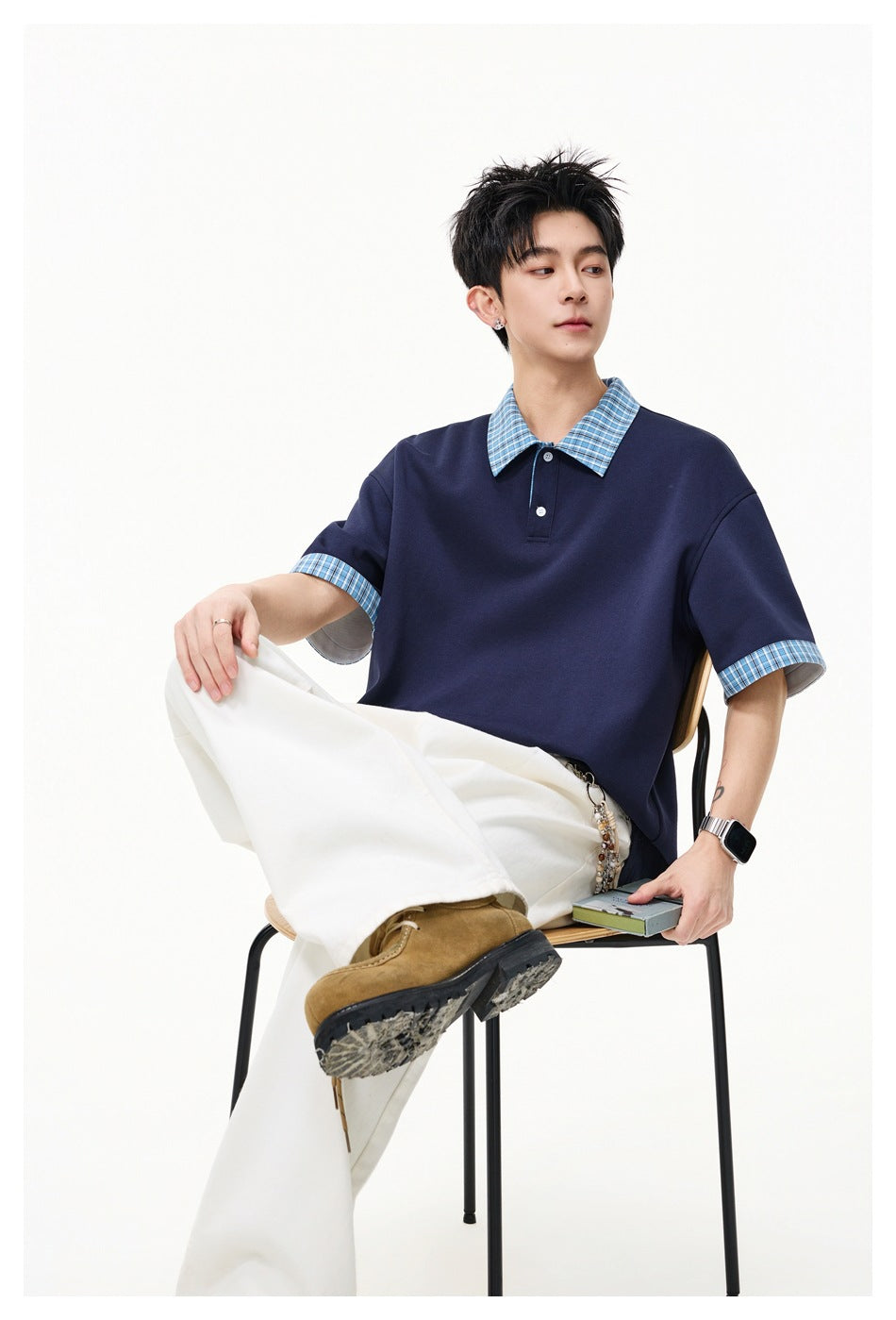Seated model wearing a navy short-sleeve polo with a blue plaid collar and cuffs.