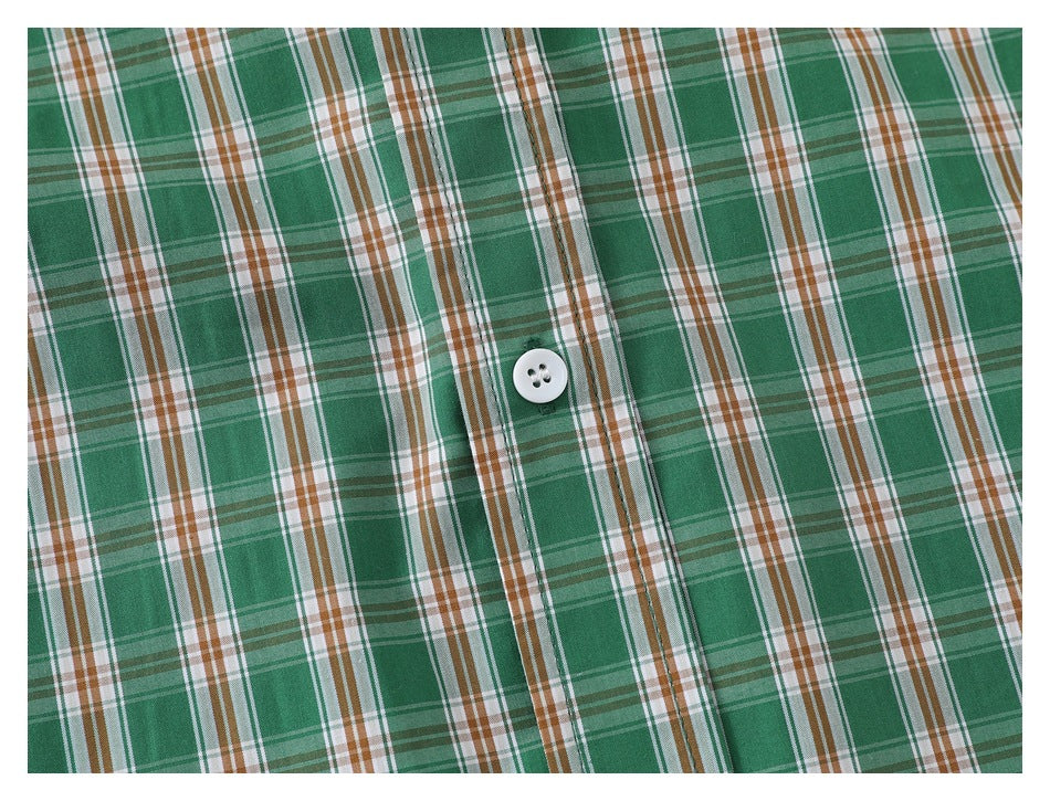 Close-up of a white button on the placket of a green, white, and brown plaid shirt.