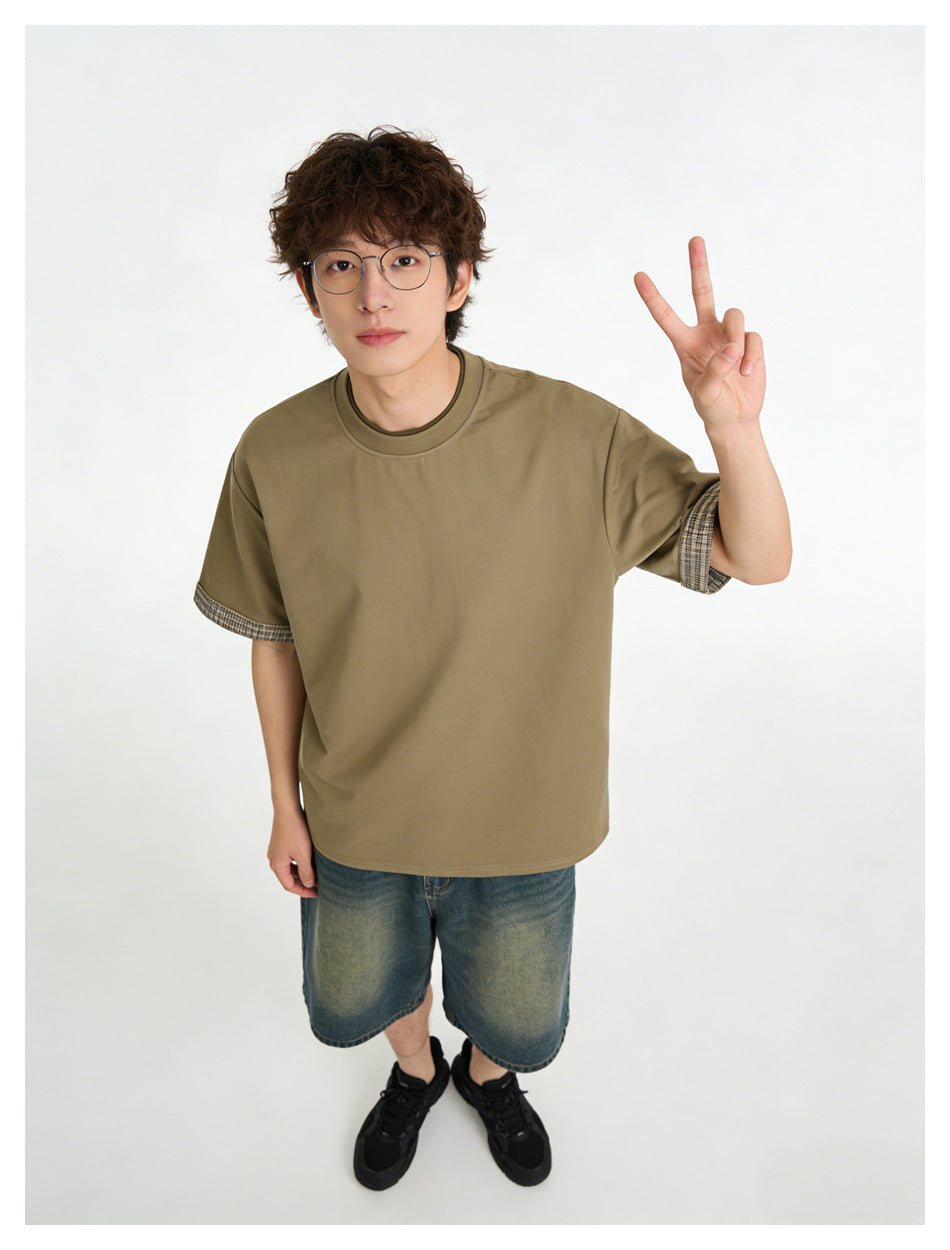 Model wearing an olive-khaki short-sleeve T-shirt with plaid cuff trim, shown from the front.