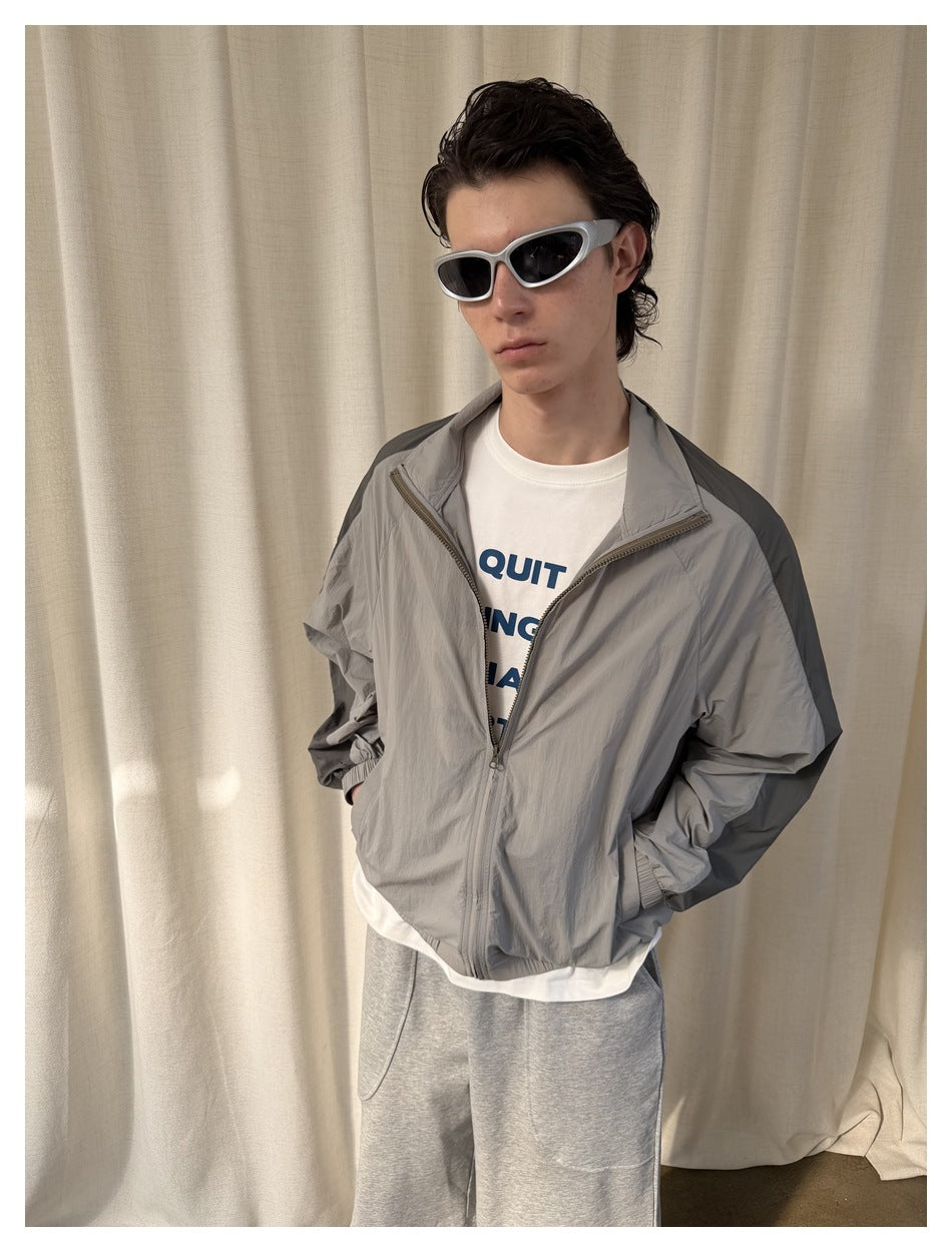 Model wearing an open light gray zip-up jacket with dark shoulder panels, showing the front and elastic hem.