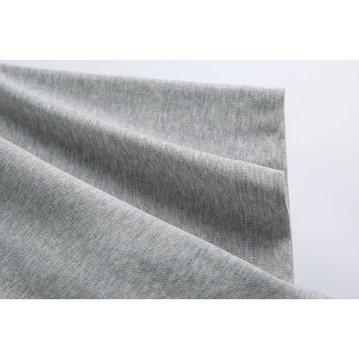 Close-up of light gray fabric folded to show its texture and stitched edges.