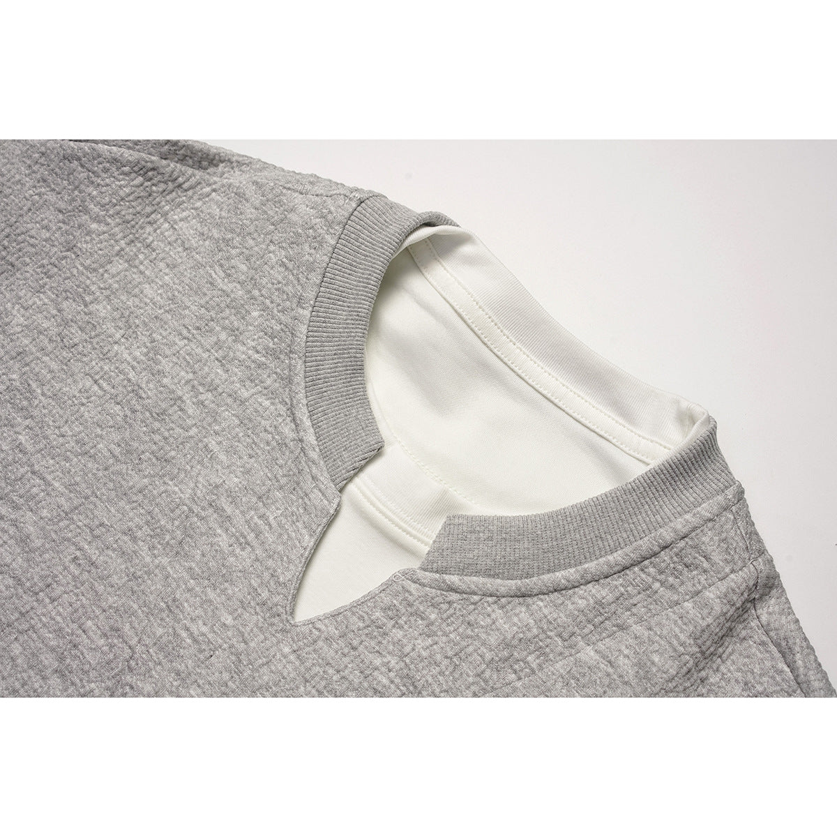 Close-up of a gray textured sweatshirt neckline layered over a white shirt.